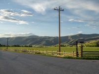 a lone country road is in the countryside area with mountains on both sides and barbed fence between the two sides