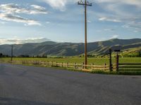 a lone country road is in the countryside area with mountains on both sides and barbed fence between the two sides