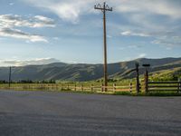 a lone country road is in the countryside area with mountains on both sides and barbed fence between the two sides