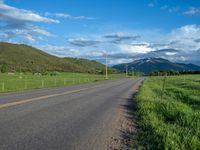 a lone country road is in the countryside area with mountains on both sides and barbed fence between the two sides