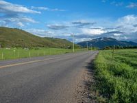 a lone country road is in the countryside area with mountains on both sides and barbed fence between the two sides