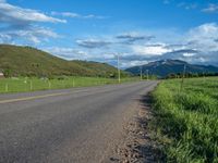 a lone country road is in the countryside area with mountains on both sides and barbed fence between the two sides