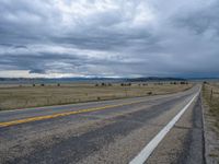 a long street passes a prairie area and mountains in the distance with heavy clouds in the sky