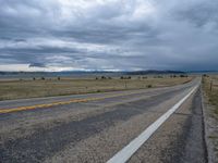 a long street passes a prairie area and mountains in the distance with heavy clouds in the sky