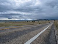 a long street passes a prairie area and mountains in the distance with heavy clouds in the sky