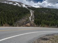 a mountain side with a road running next to the mountains, a bike parked in front of it and trees on one side