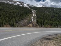 a mountain side with a road running next to the mountains, a bike parked in front of it and trees on one side