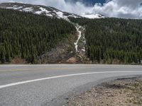 a mountain side with a road running next to the mountains, a bike parked in front of it and trees on one side