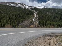 a mountain side with a road running next to the mountains, a bike parked in front of it and trees on one side