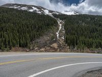 a mountain side with a road running next to the mountains, a bike parked in front of it and trees on one side