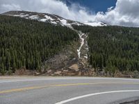 a mountain side with a road running next to the mountains, a bike parked in front of it and trees on one side