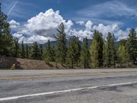 road in the mountains with pine trees and mountains in the background with blue sky with fluffy clouds