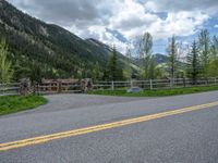 road in the mountains with grass and trees and a fence surrounding it on a bright day