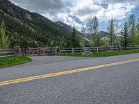 road in the mountains with grass and trees and a fence surrounding it on a bright day