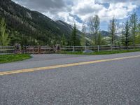 road in the mountains with grass and trees and a fence surrounding it on a bright day