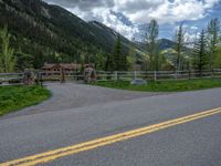 road in the mountains with grass and trees and a fence surrounding it on a bright day