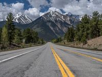 road in the mountains with pine trees and mountains in the background with blue sky with fluffy clouds