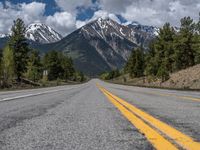 road in the mountains with pine trees and mountains in the background with blue sky with fluffy clouds