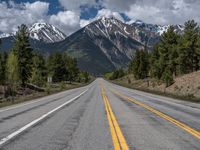 road in the mountains with pine trees and mountains in the background with blue sky with fluffy clouds