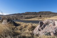 a mountain road with a lone rock next to it on the ground is empty and yellow dry grass