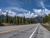 road in the mountains with pine trees and mountains in the background with blue sky with fluffy clouds