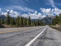 road in the mountains with pine trees and mountains in the background with blue sky with fluffy clouds