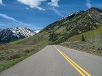 the road is paved with yellow markings and has a snowy mountain range in the background