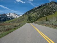 the road is paved with yellow markings and has a snowy mountain range in the background