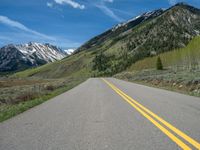 the road is paved with yellow markings and has a snowy mountain range in the background