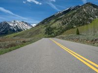 the road is paved with yellow markings and has a snowy mountain range in the background