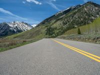 the road is paved with yellow markings and has a snowy mountain range in the background