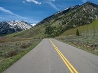 the road is paved with yellow markings and has a snowy mountain range in the background