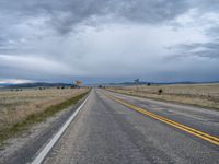 a long street passes a prairie area and mountains in the distance with heavy clouds in the sky