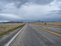 a long street passes a prairie area and mountains in the distance with heavy clouds in the sky