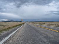 a long street passes a prairie area and mountains in the distance with heavy clouds in the sky