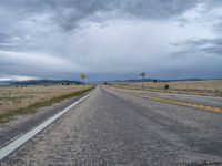 a long street passes a prairie area and mountains in the distance with heavy clouds in the sky