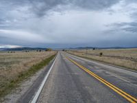 a long street passes a prairie area and mountains in the distance with heavy clouds in the sky