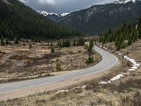 a mountain side with a road running next to the mountains, a bike parked in front of it and trees on one side