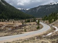 a mountain side with a road running next to the mountains, a bike parked in front of it and trees on one side