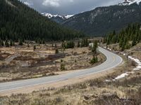 a mountain side with a road running next to the mountains, a bike parked in front of it and trees on one side