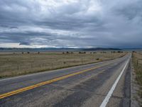 a long street passes a prairie area and mountains in the distance with heavy clouds in the sky