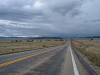 a long street passes a prairie area and mountains in the distance with heavy clouds in the sky