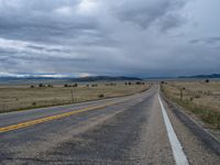 a long street passes a prairie area and mountains in the distance with heavy clouds in the sky