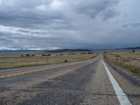 a long street passes a prairie area and mountains in the distance with heavy clouds in the sky