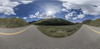 an upside down lens view shows a wide open road between green trees and mountains with snow in the background