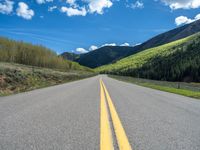 the road is paved with yellow markings and has a snowy mountain range in the background