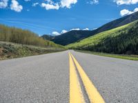 the road is paved with yellow markings and has a snowy mountain range in the background