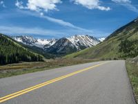 the road is paved with yellow markings and has a snowy mountain range in the background