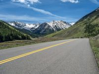 the road is paved with yellow markings and has a snowy mountain range in the background