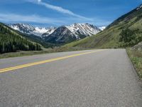 the road is paved with yellow markings and has a snowy mountain range in the background